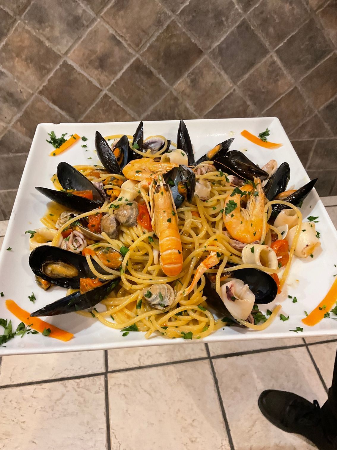 Piatto di pasta ai frutti di mare con cozze, gamberi e calamari su un piatto rettangolare bianco.