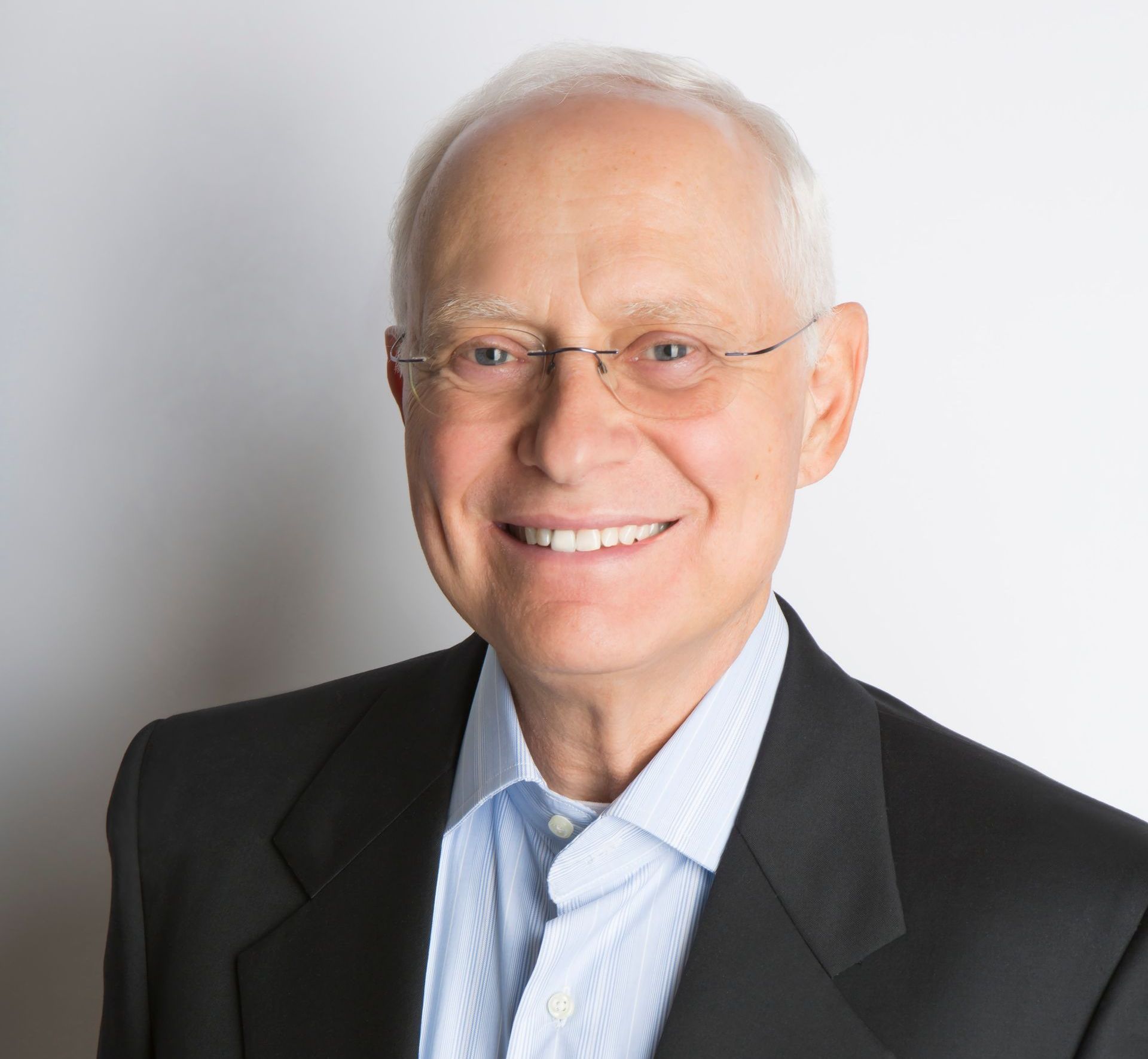 A man wearing glasses and a suit is smiling for the camera