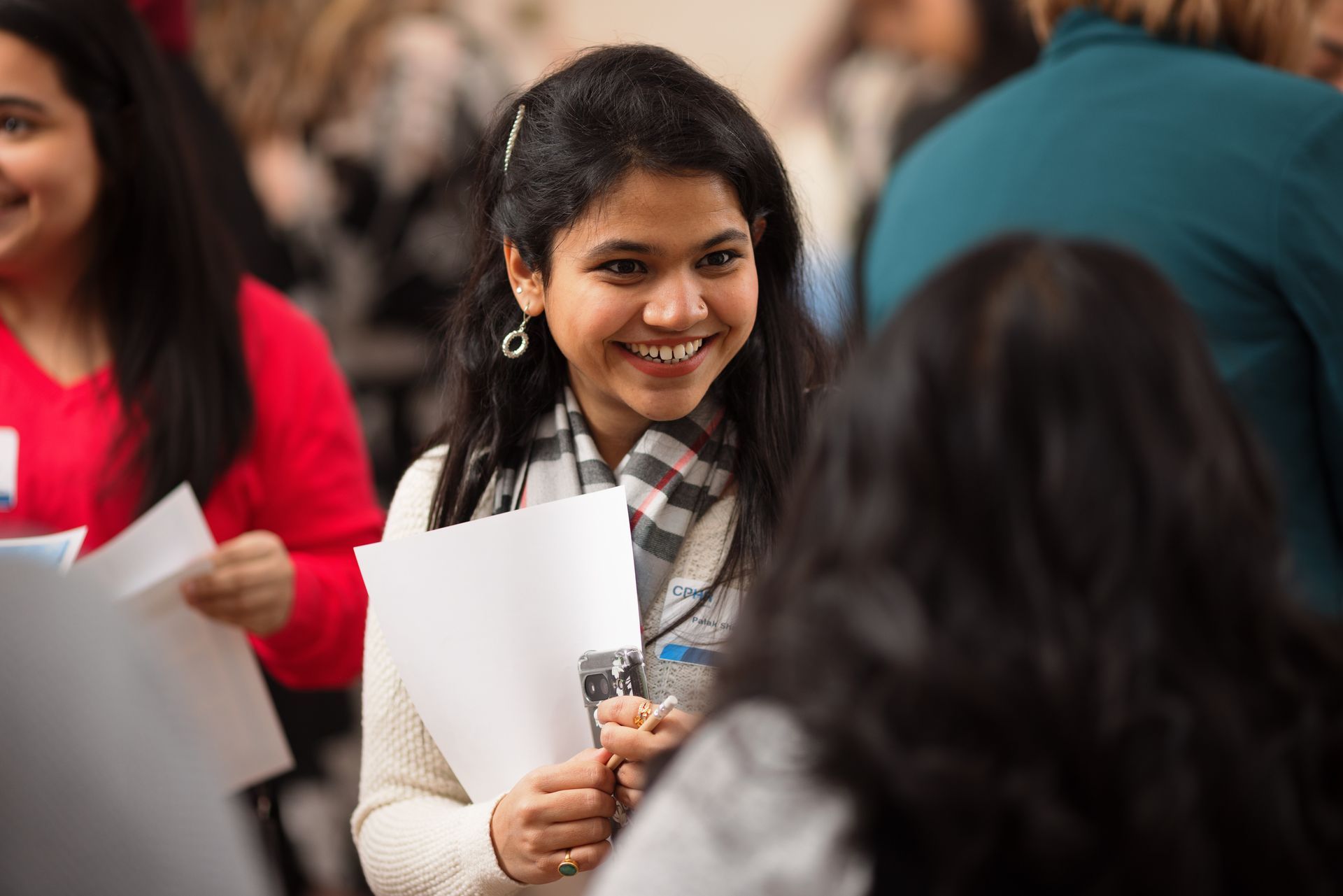 A woman is smiling while holding a piece of paper in her hand.