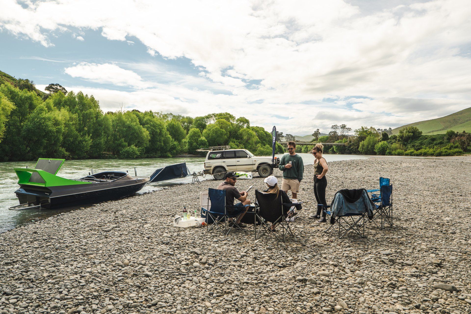 A group of people are sitting on a rocky beach near a river