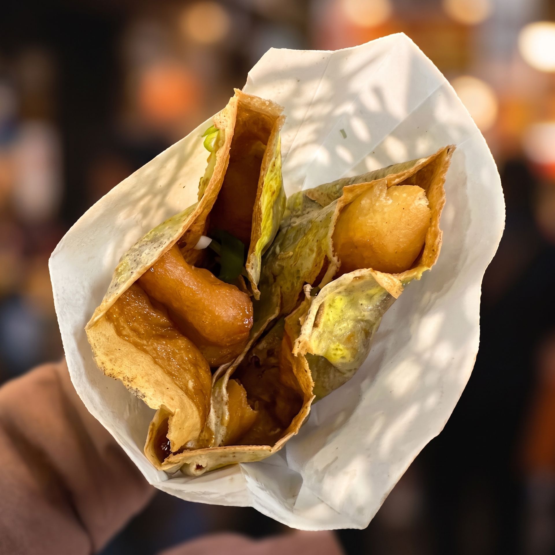 Open paper cone holding fried snacks with green chutney, against a blurred background