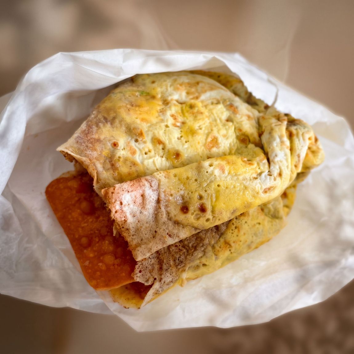 Folded omelet sandwich in white paper wrapper, with visible red filling inside.