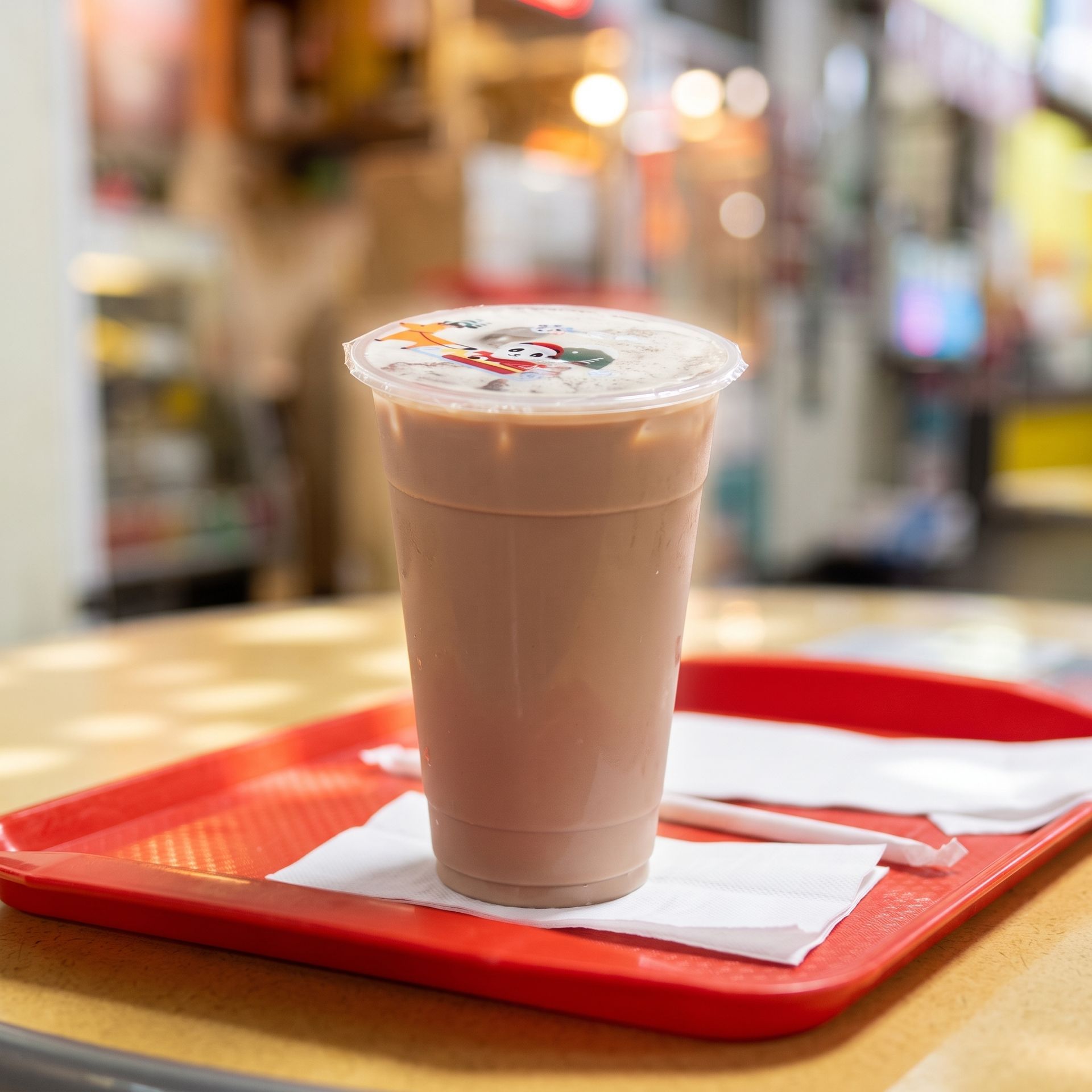 Iced drink in a clear cup on a red tray, placed on a napkin in a bright café setting.