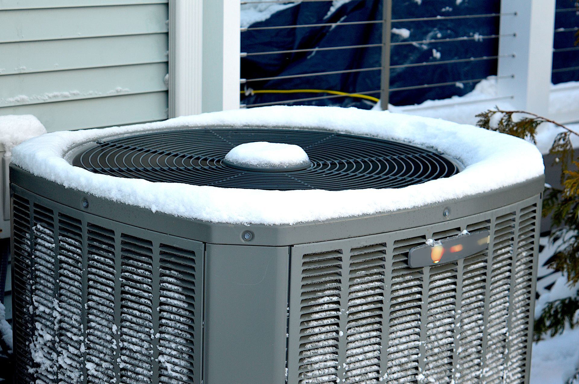 Air conditioning unit covered in snow outside a house.