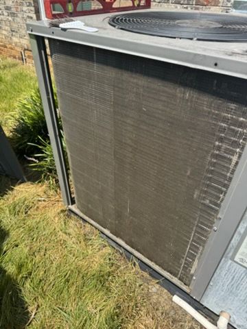 HVAC technician connecting gauges to an AC unit. Blue and red gauges, a fan, and blue clothing are visible.