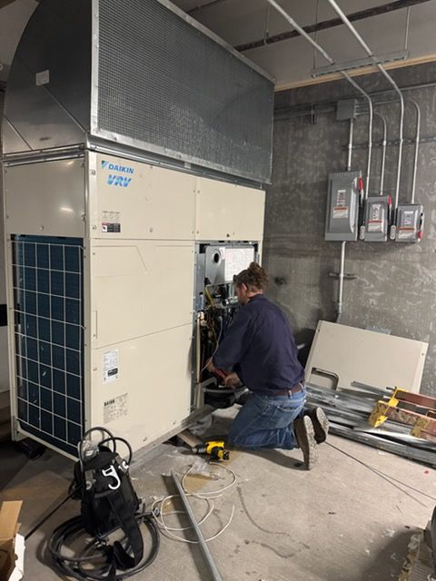 Two HVAC technicians in safety gear work on rooftop units.