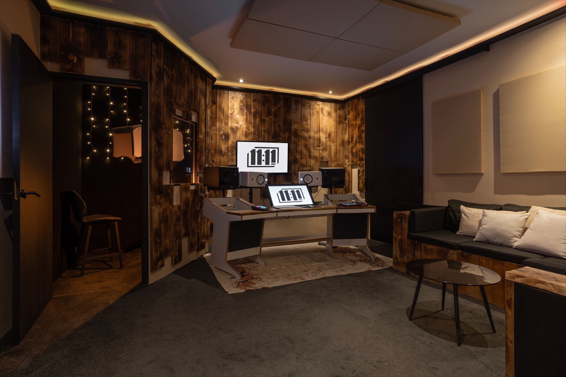Music studio: desk with equipment, recording booth doorway, and seating area with sofa.
