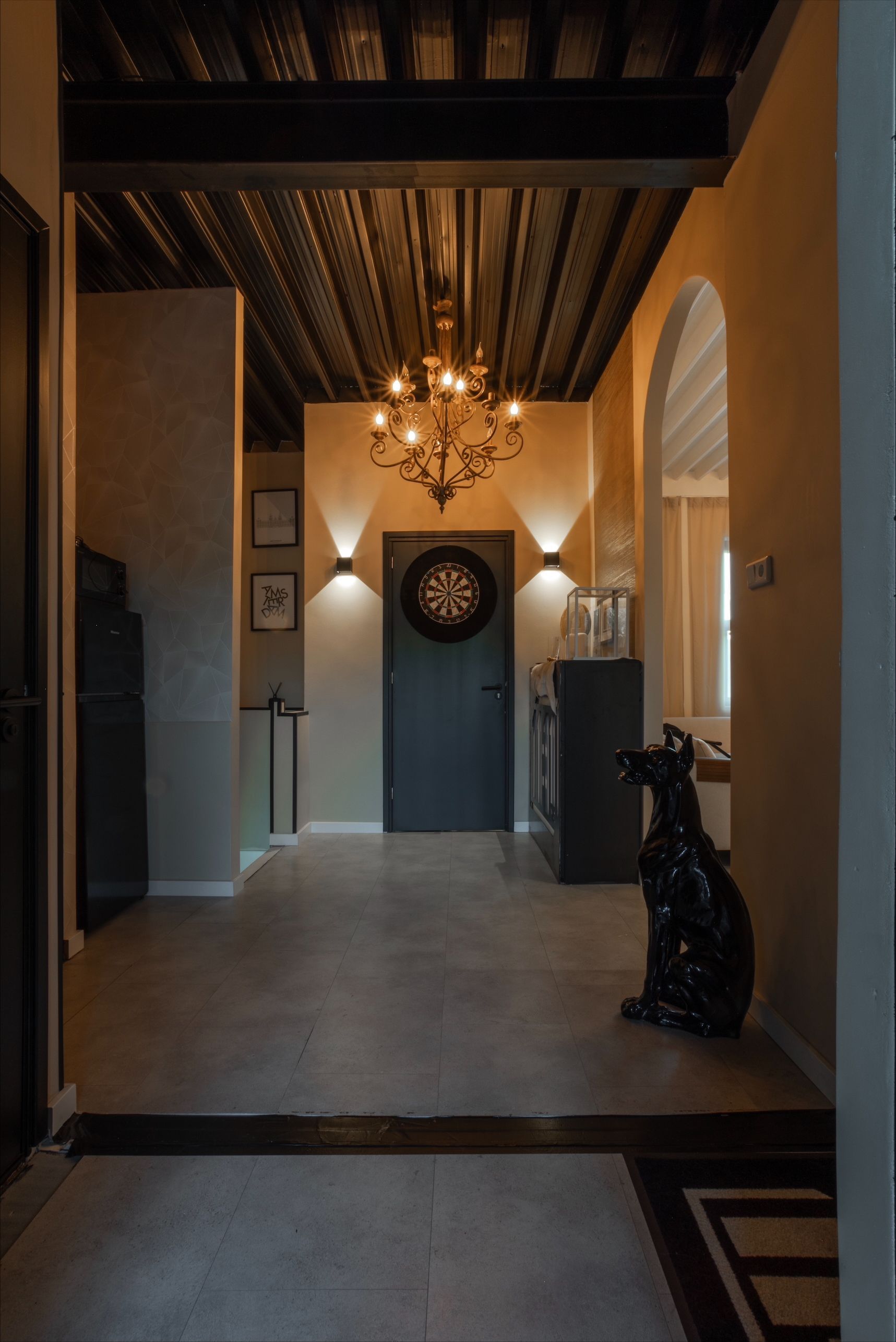 Hallway with dark ceiling, chandelier, dark door, archway, dog statue.