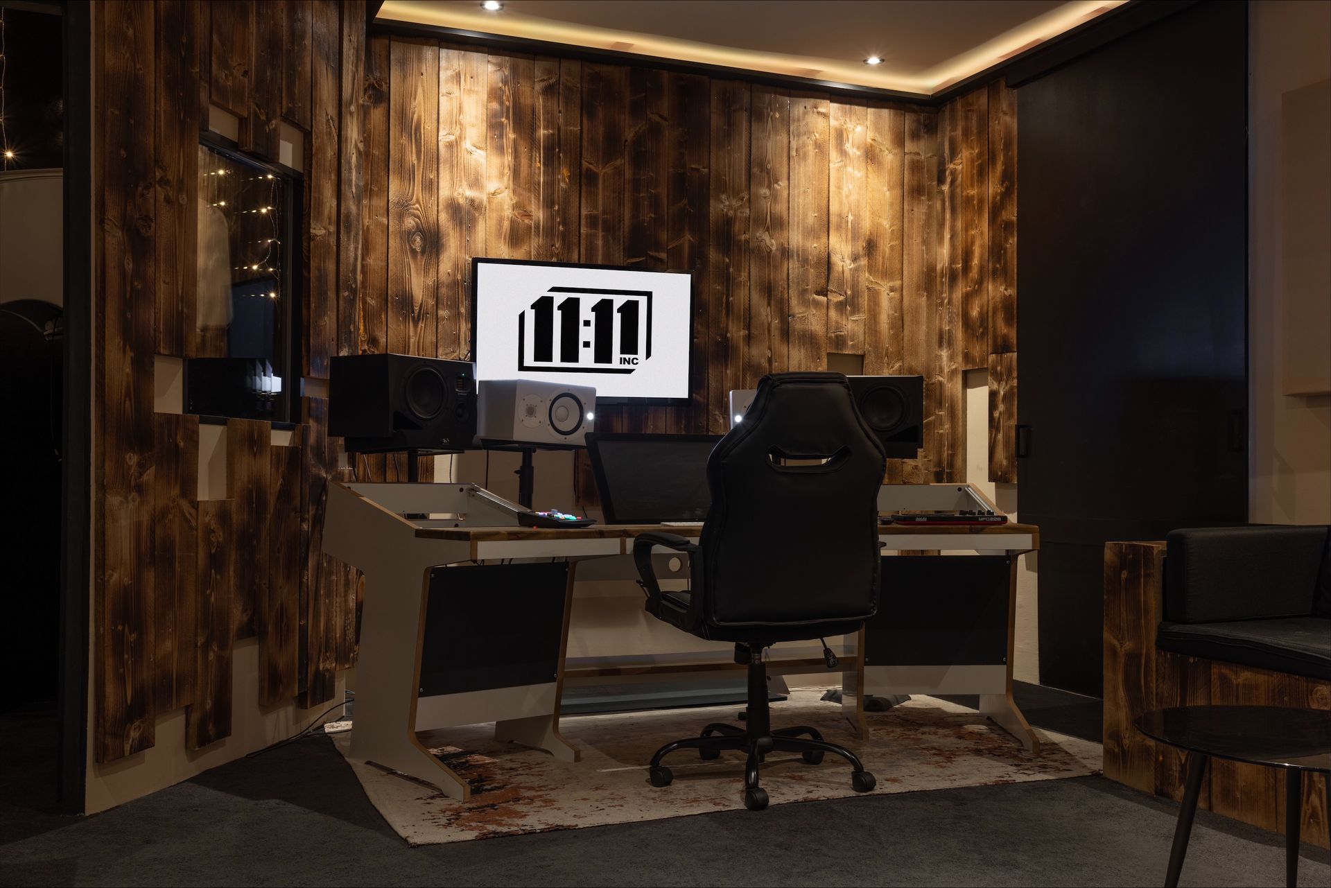 Music studio with wood paneling, a desk with equipment, a black chair, and a screen showing 