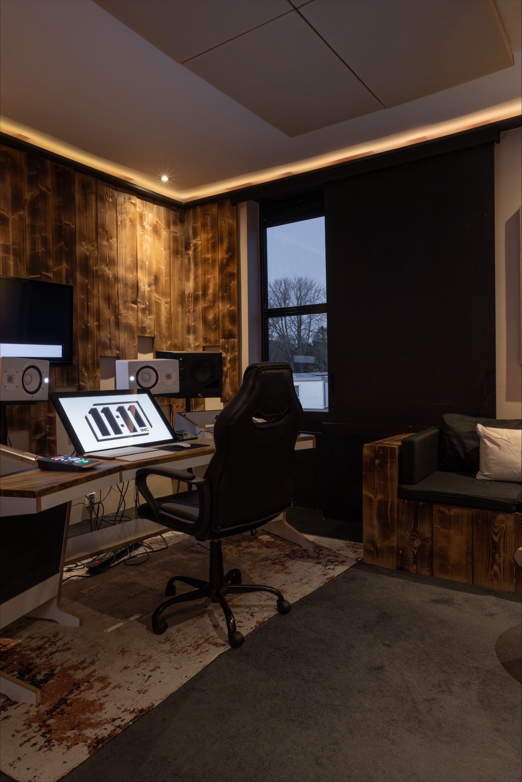 Music studio interior with a desk, monitors, keyboard display, and a window with a view.
