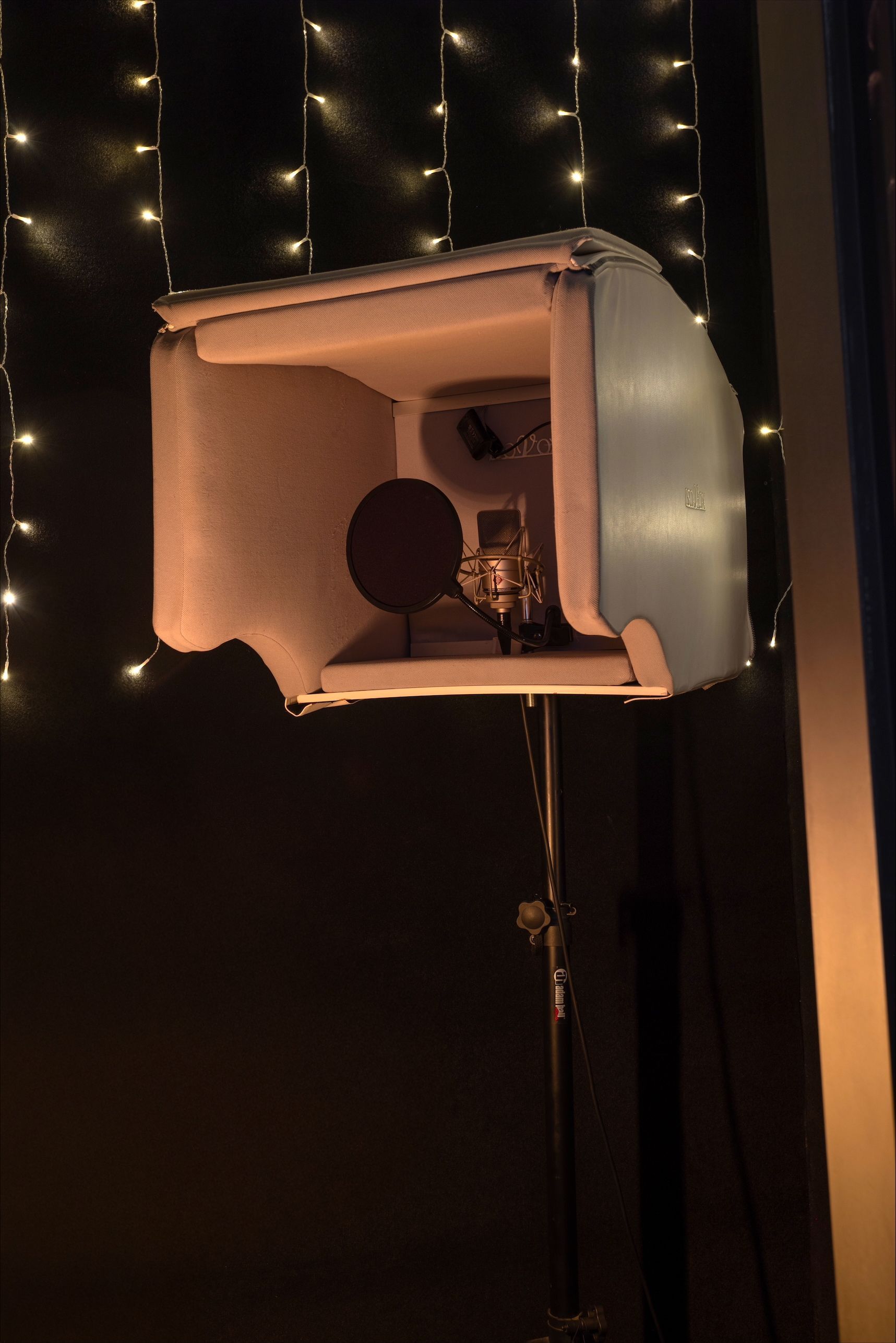 A microphone in a soundproof box, lit by warm light, against a backdrop of fairy lights.