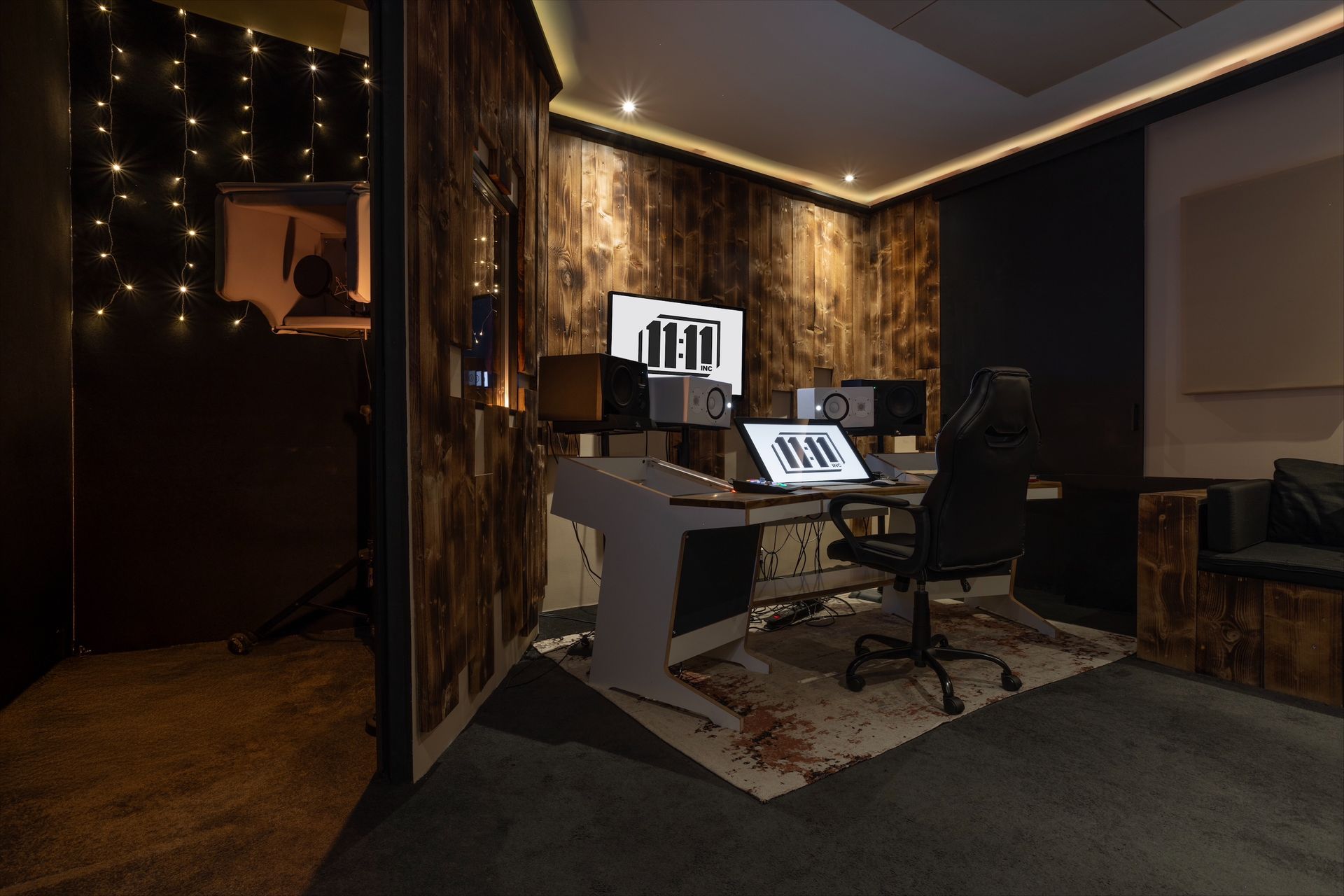 Recording studio interior with wooden walls, a desk with monitors, and a vocal booth on the left.
