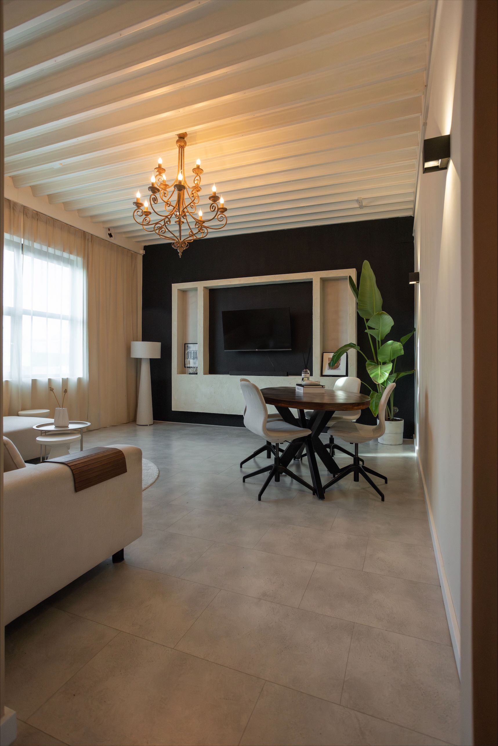 Living room with black accent wall, chandelier, dining table, and sofa.