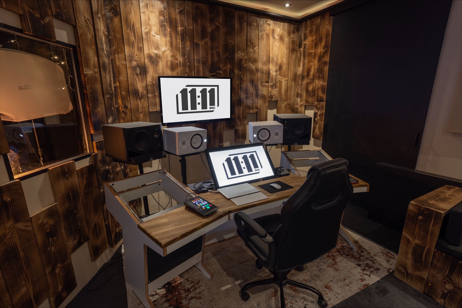 Recording studio with desk, monitors, and a black chair. Wooden walls and carpet.
