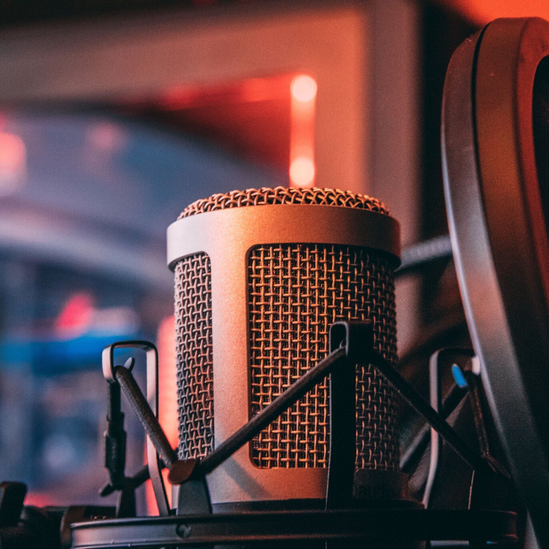 Close-up of a silver microphone in a studio setting with red and orange lighting.