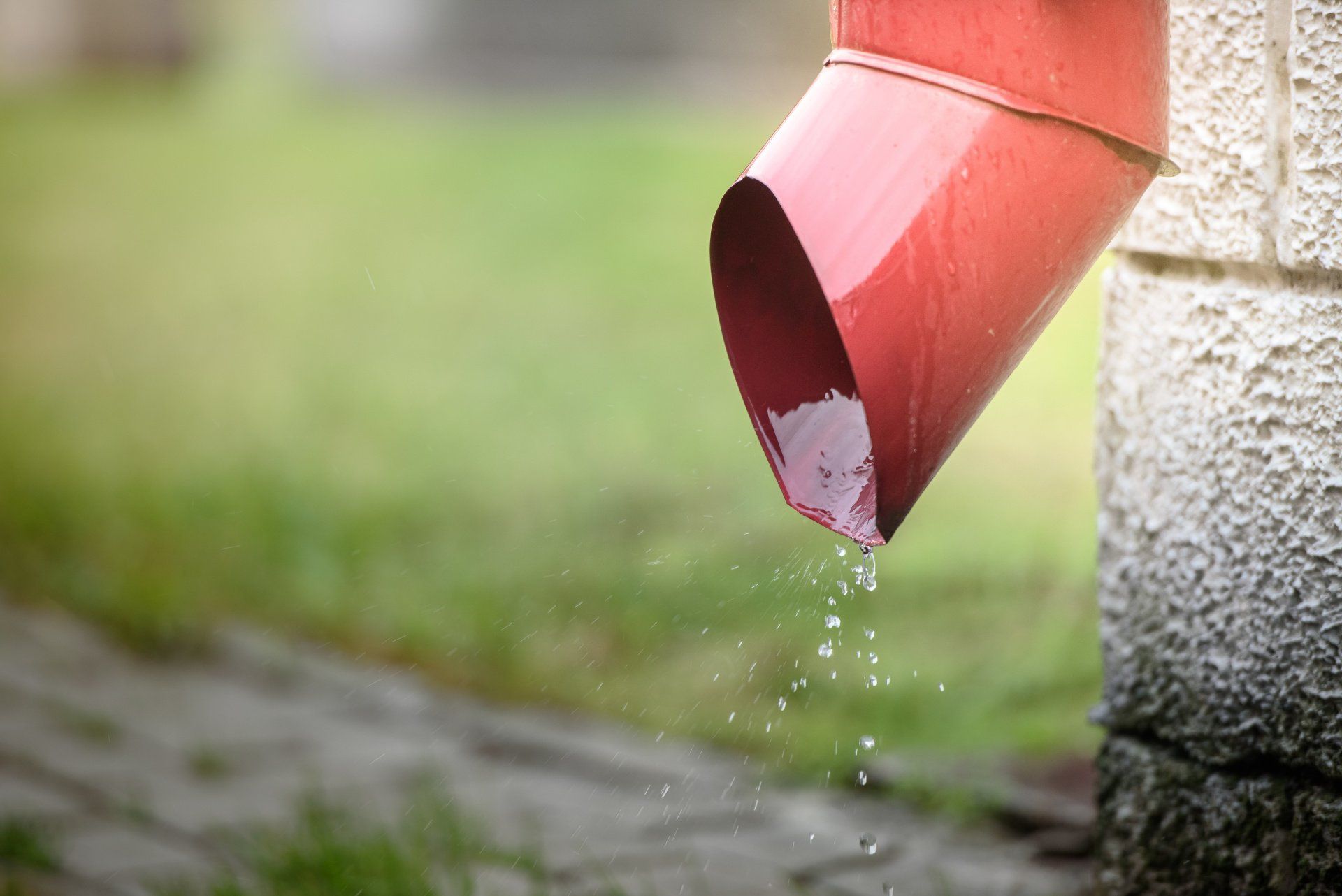 Water is coming out of a red gutter on a brick wall.