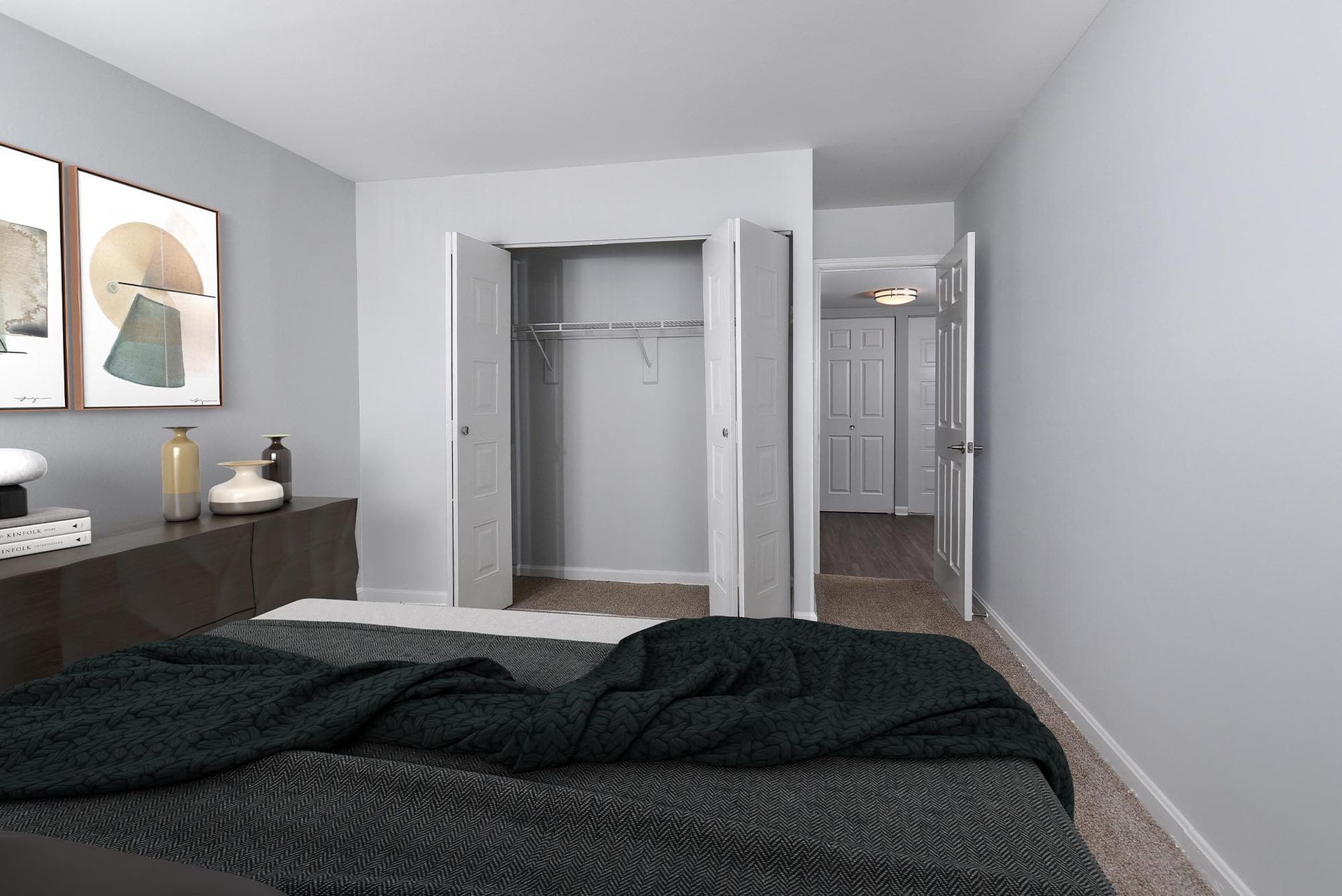 Bedroom with a dark blanket on the bed, a closet, a dresser with artwork, and a hallway at Glenmont Station in Silver Spring, MD.