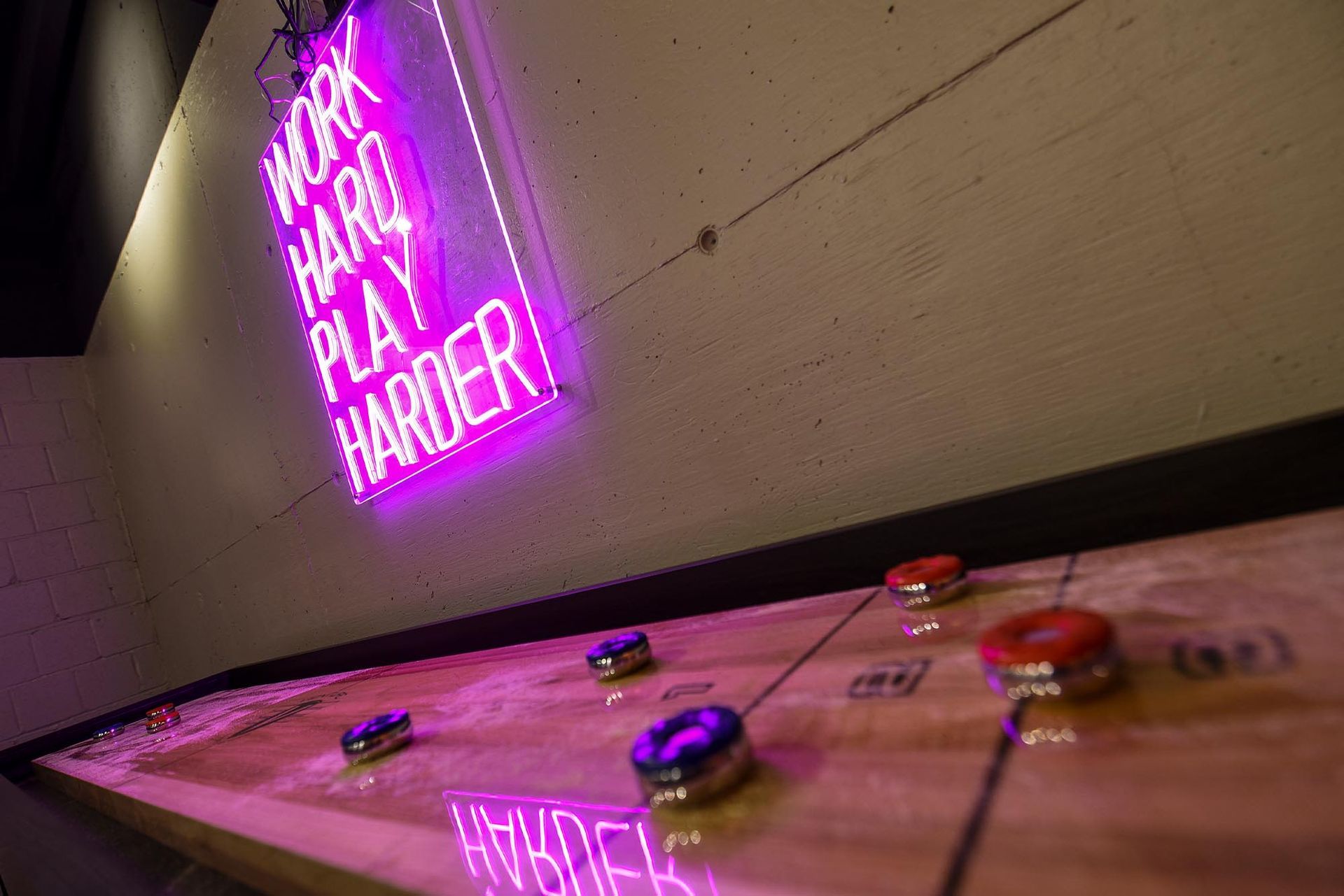 Shuffleboard table lit by neon sign: