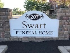 Sign for Swart Funeral Home at 207, white with black lettering, set between brick columns.