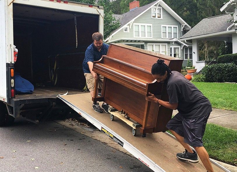 Two men are carrying a piano out of a truck.