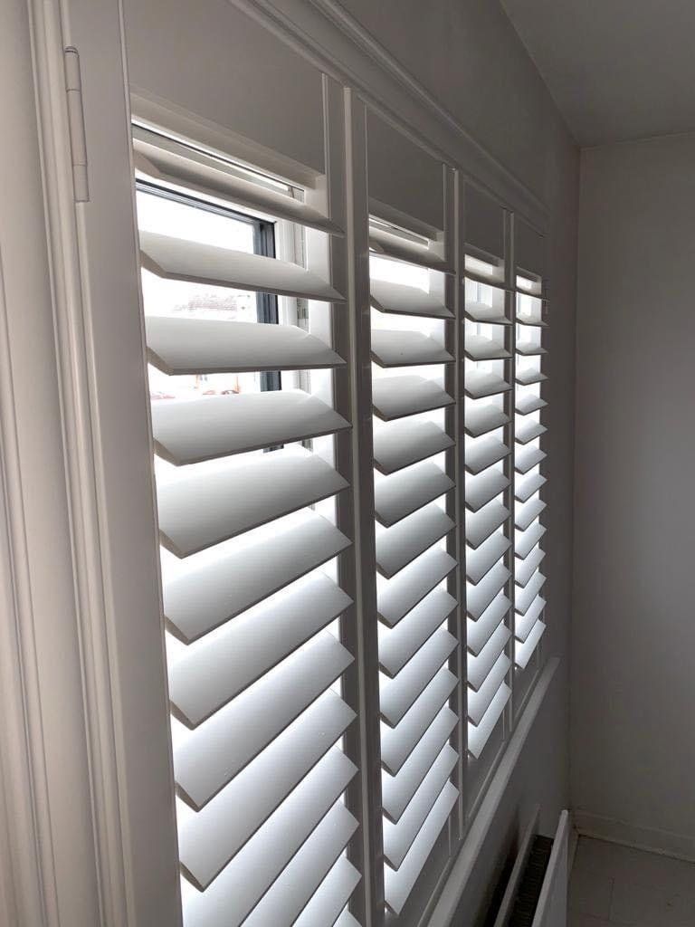 A window with white shutters on it in a room.