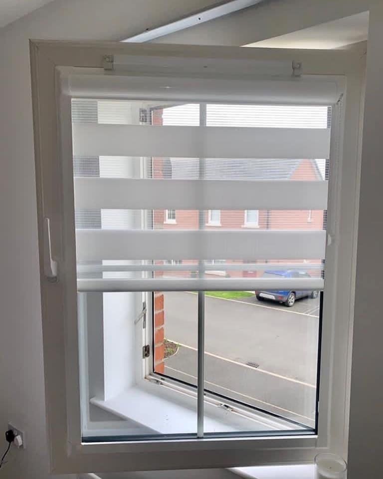 A window with a blind on it and a view of a street.