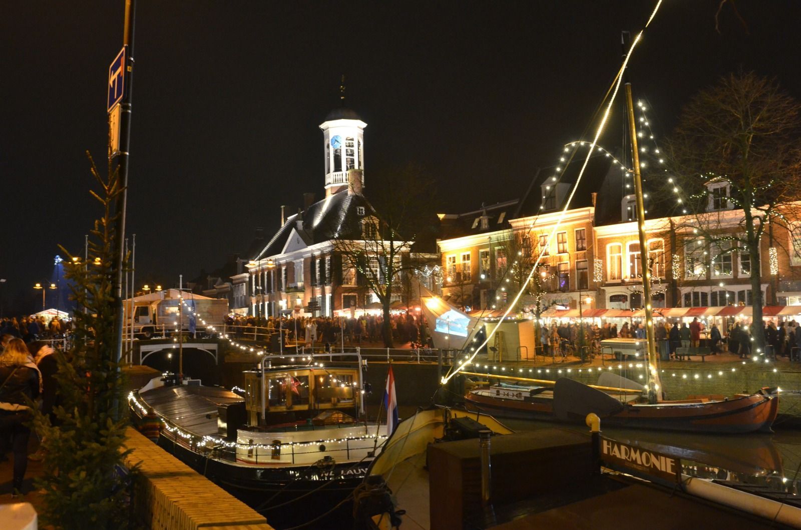 Nachtelijke haven met verlichte gebouwen en zeilboten die in het water weerspiegelen.