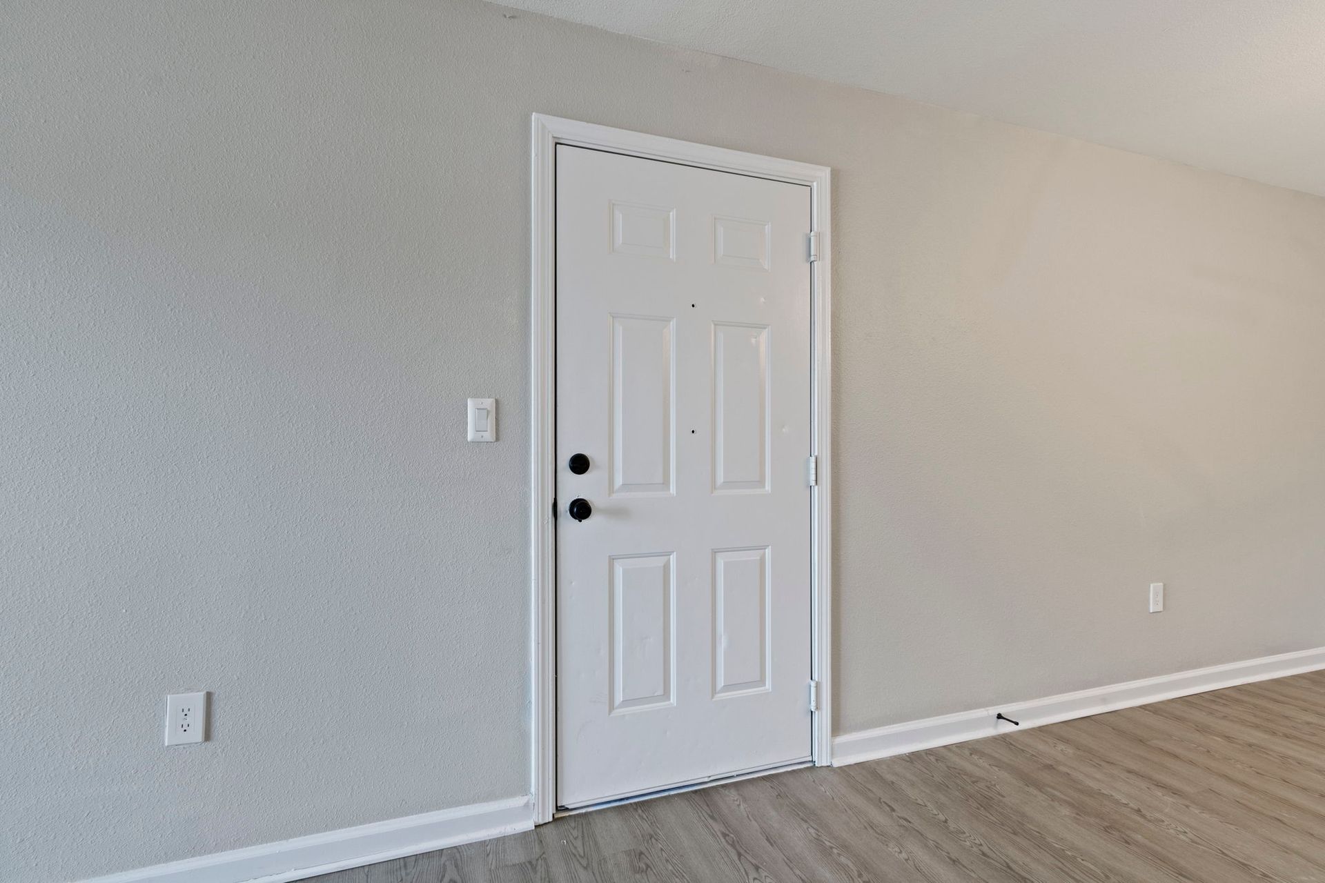 White door in a room with light gray textured walls and wood-look flooring.