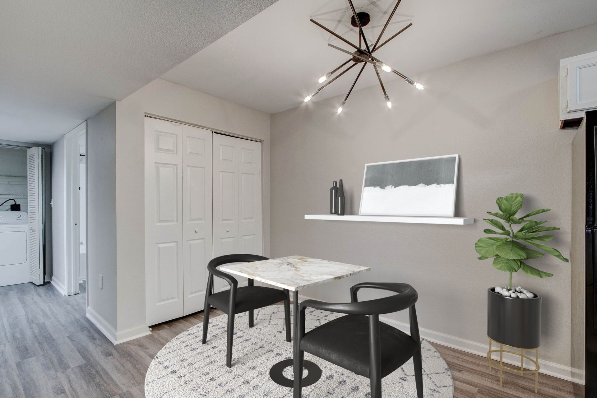 Dining area with a table, two chairs, a rug, and a shelf with decor.