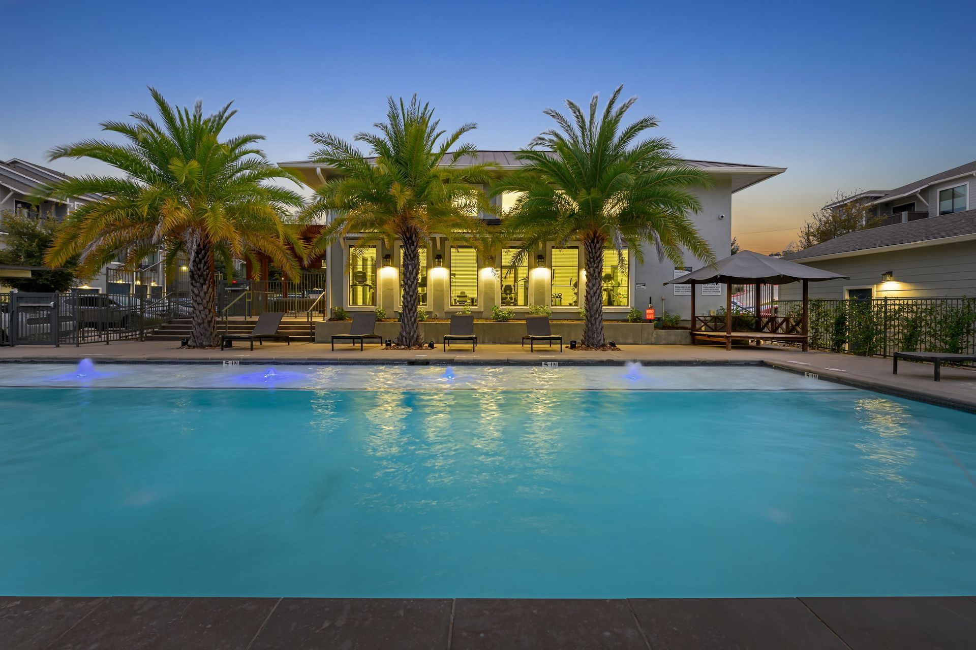 A large swimming pool surrounded by palm trees in front of the apartment building at Marquis SoCo in South Austin, TX.