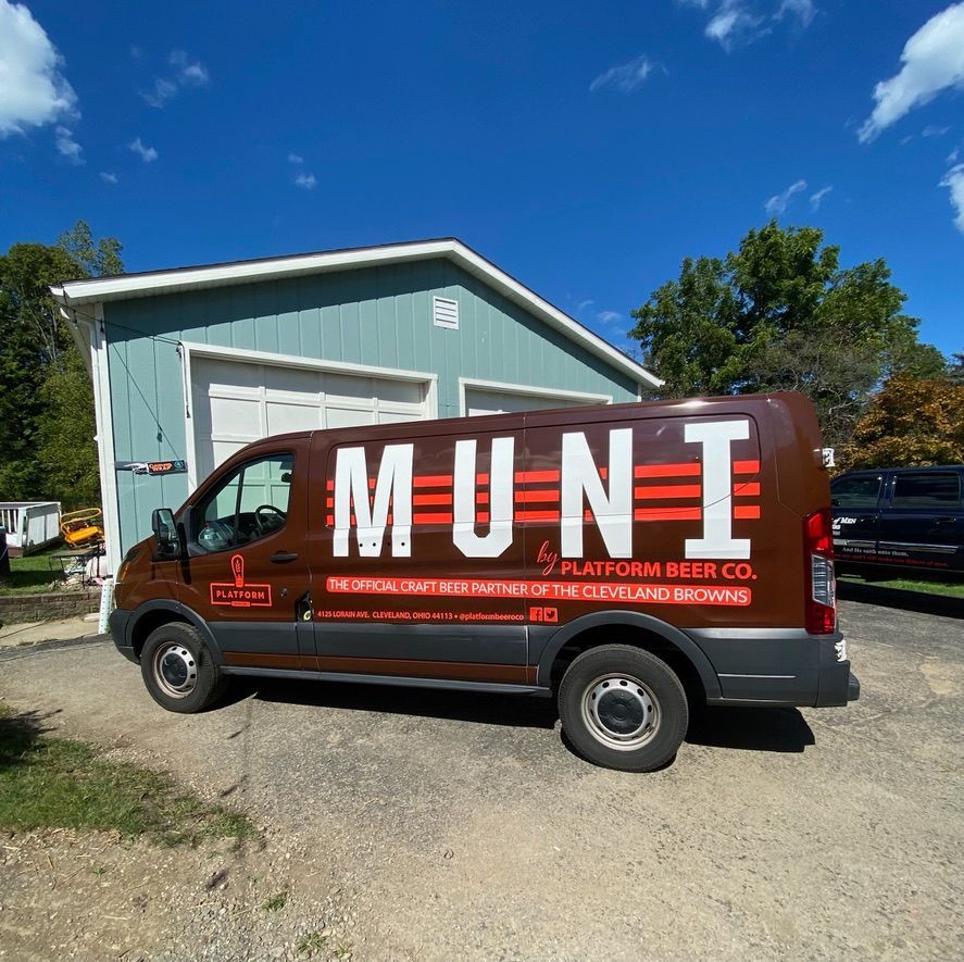 Dark red Mune delivery van parked by a light blue building under a bright blue sky