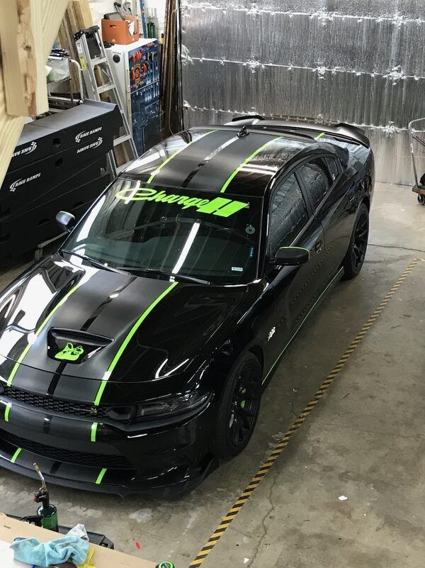 Black sports car with neon green racing stripes parked in a garage