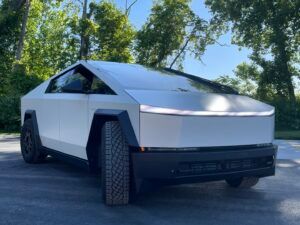 White futuristic electric pickup truck parked outdoors on a tree-lined street.
