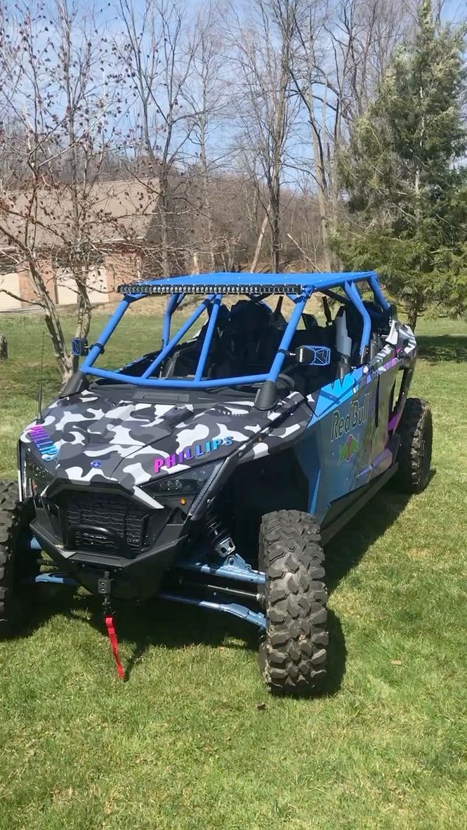 Camouflaged off-road side-by-side with blue roll cage parked on a grassy lawn