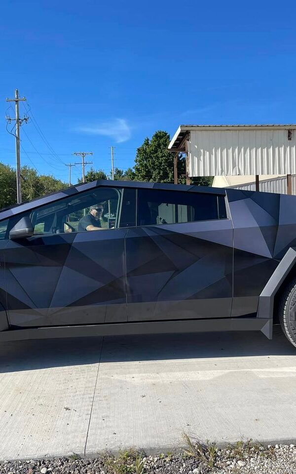 Black geometric-patterned car parked on a sunny street beside a building and utility poles