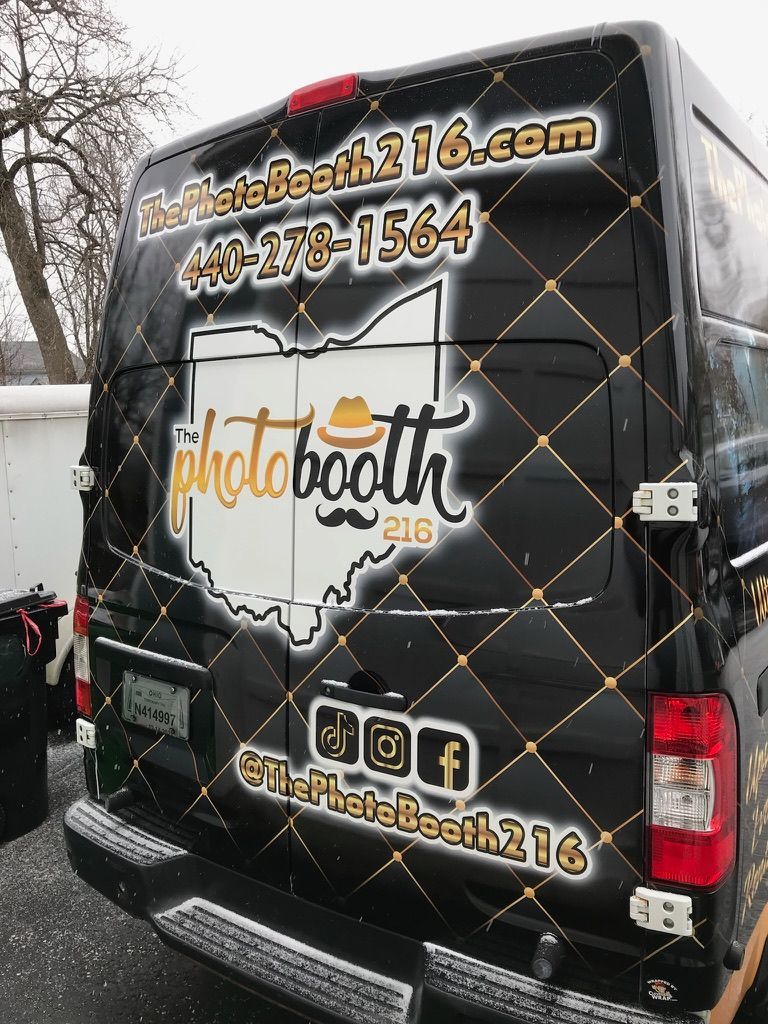 Black photo booth van with gold lettering parked outdoors in a snowy lot