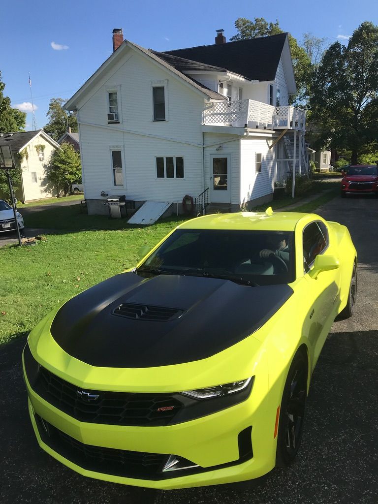 Neon yellow sports car with black hood parked on grass in front of a white house