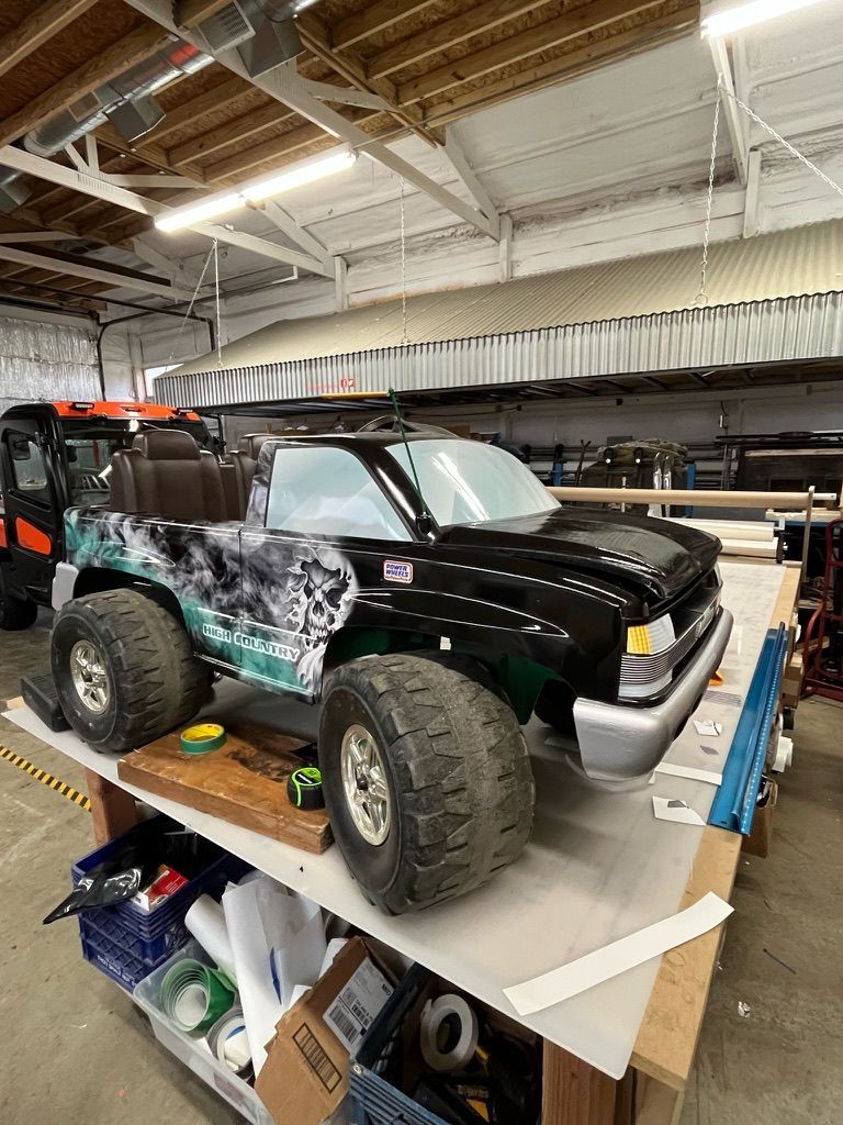 Black RC off-road truck on a workbench in a garage, with tools and boxes nearby.