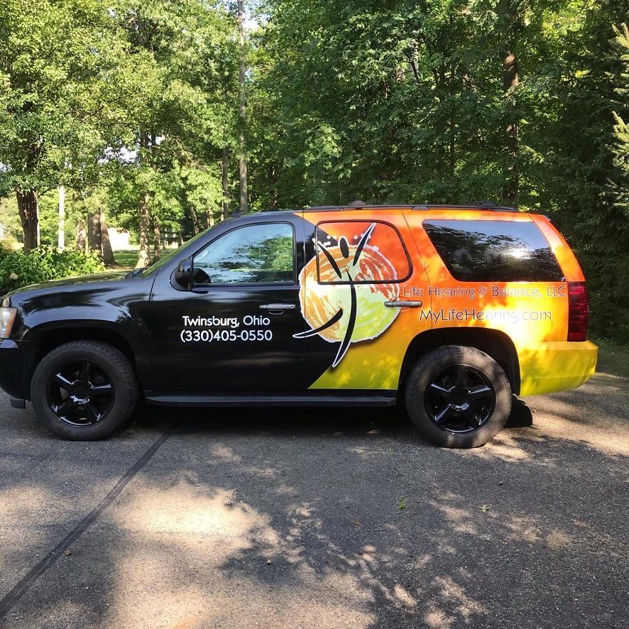 Black-and-orange wrapped service SUV parked on a wooded roadside, with company contact text on the door
