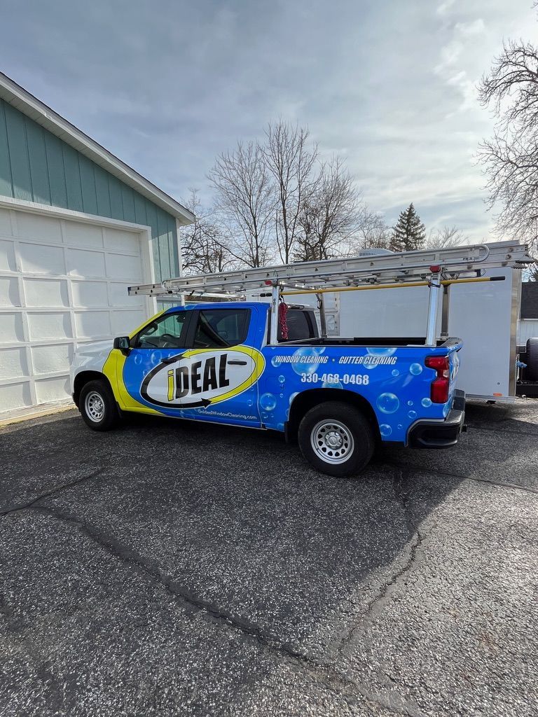 Blue IDEAL service truck parked beside a garage in a driveway on a cloudy day