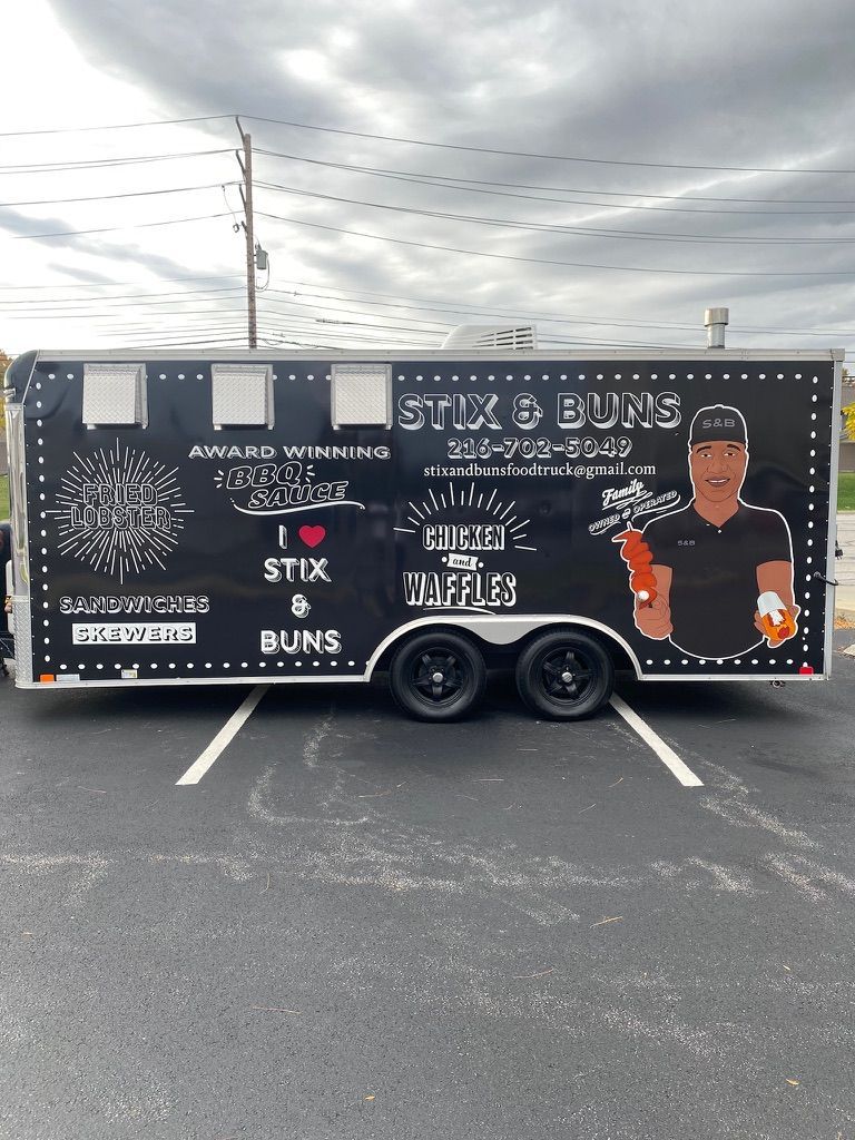 Black food trailer with menu graphics and a man holding a drink in a parking lot