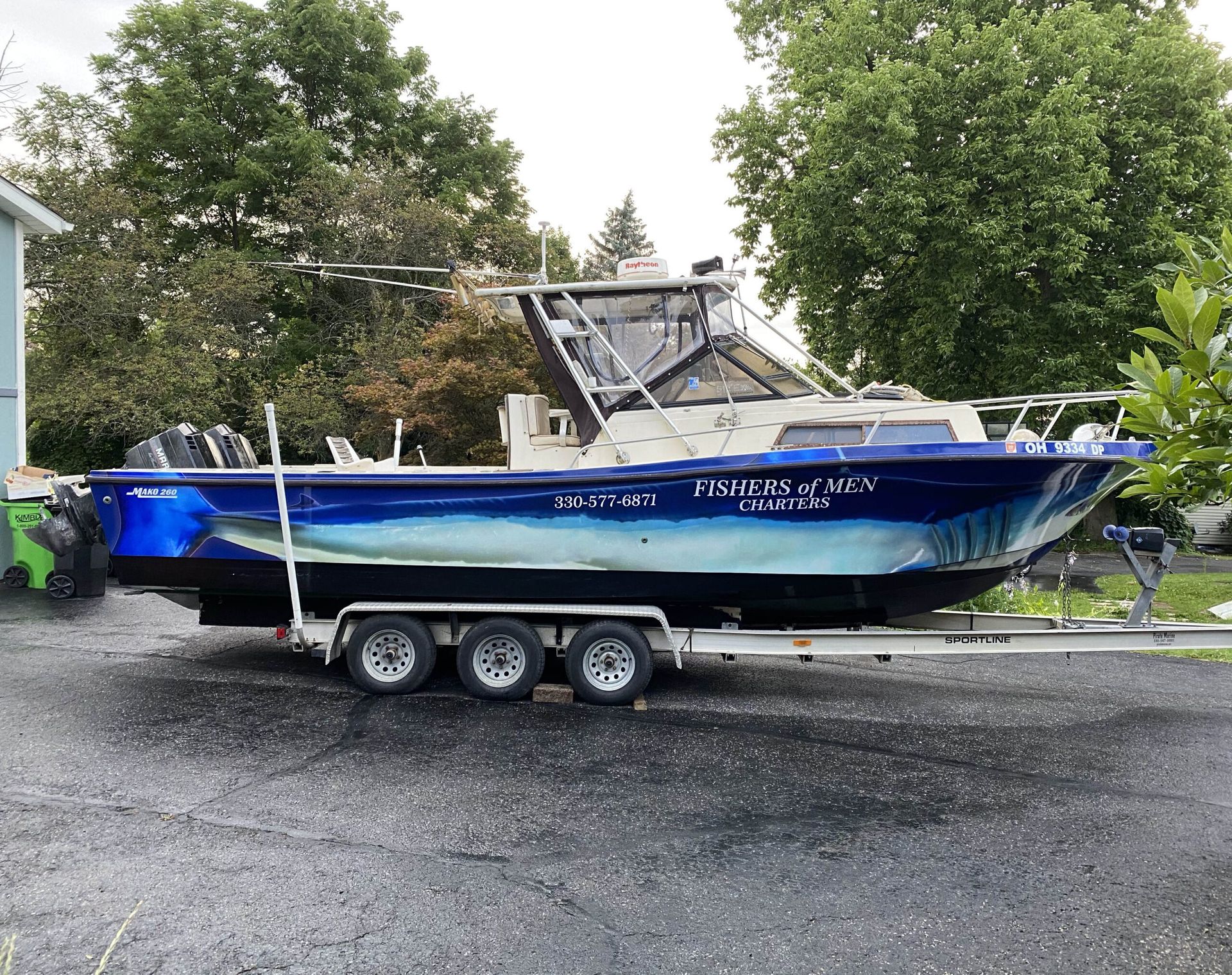 Blue fishing boat on a trailer in a parking lot with trees in the background