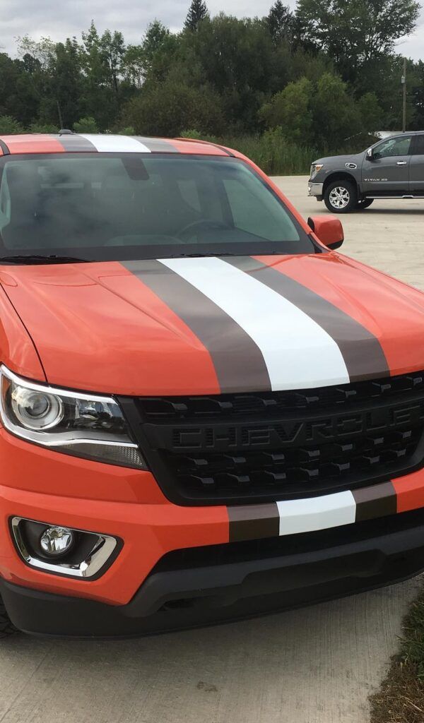Orange sports car with black and white racing stripes parked outdoors in a lot
