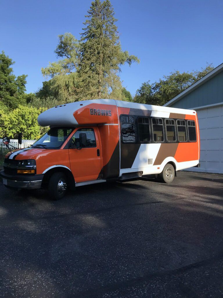 Orange and white shuttle bus parked on a sunny street beside a building and trees