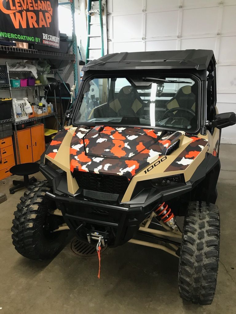 Camouflage UTV with large off-road tires parked inside a garage or shop