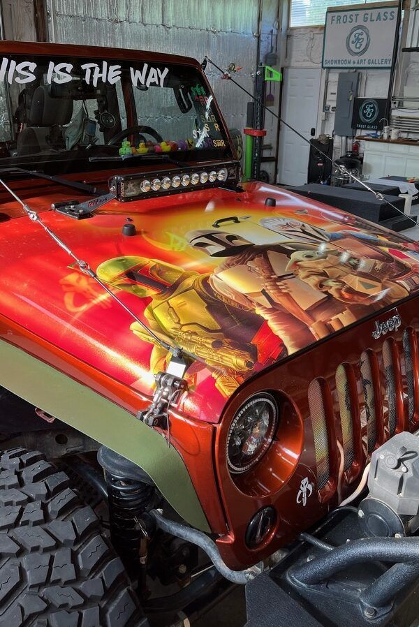Red Jeep with colorful hood artwork and “This is the way” windshield text in a garage
