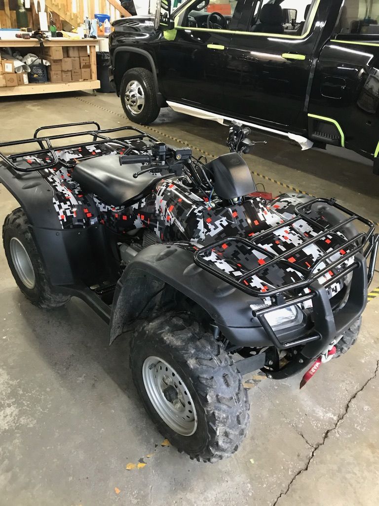 Black ATV in a garage with exposed wiring, parked beside a black pickup truck.