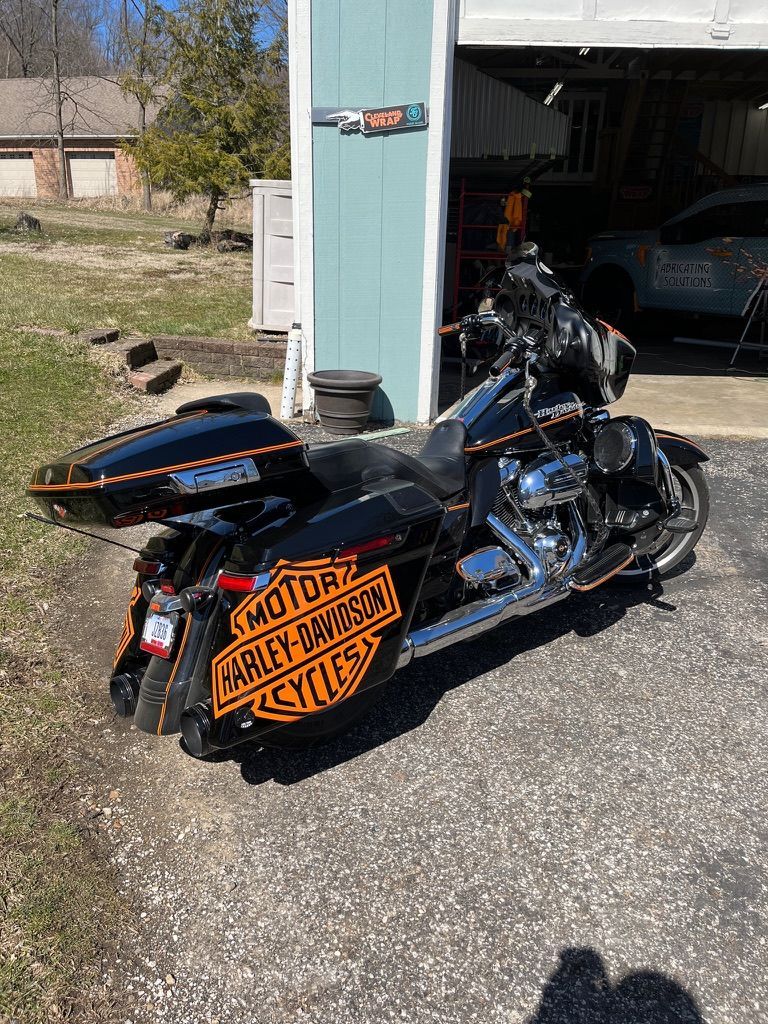 Black motorcycle with orange side sign parked in a garage driveway, front wheel turned outward