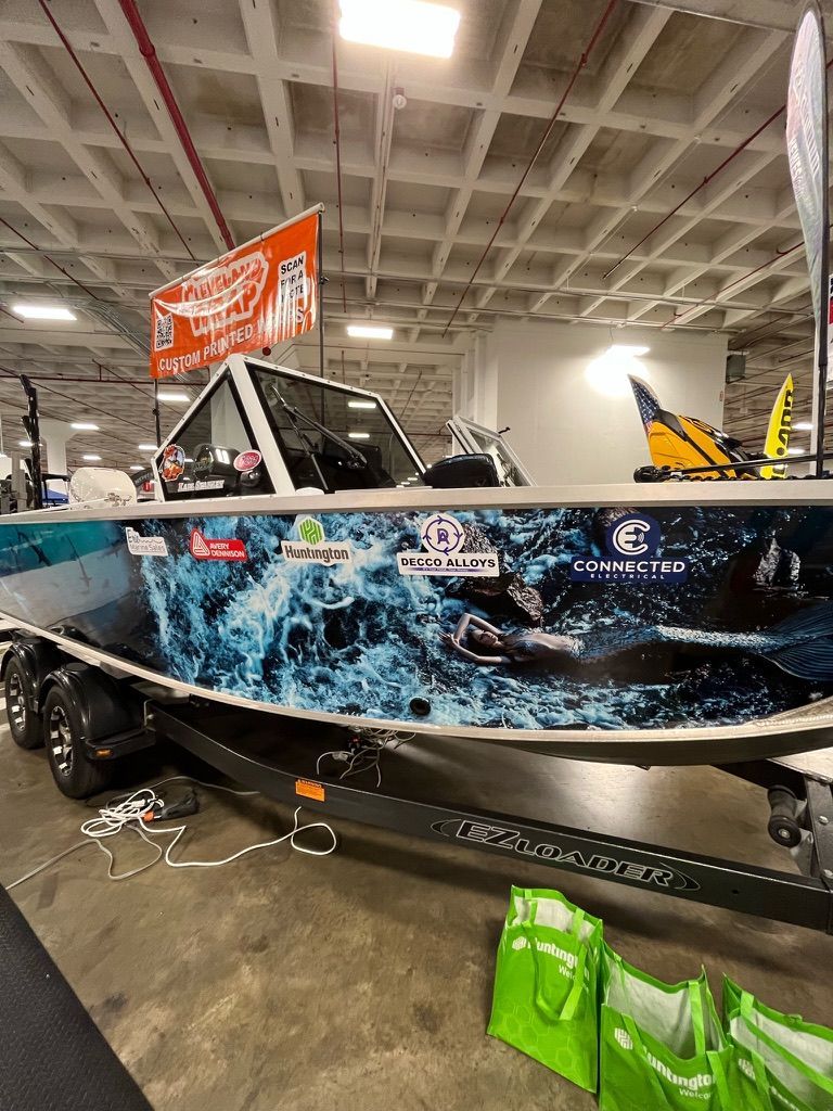 Black boat with blue shark wrap displayed indoors at a boat show.