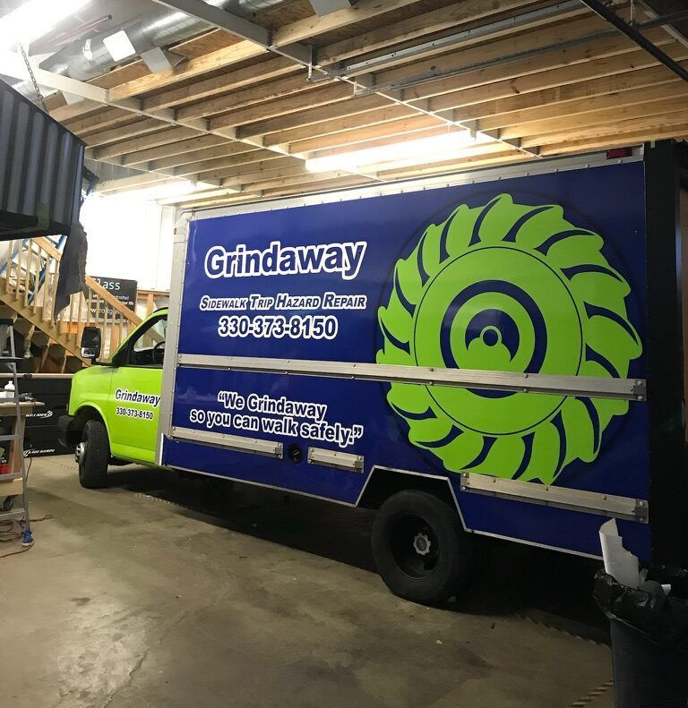 Blue GrinAway truck with large green logo parked inside a garage with exposed wooden ceiling beams